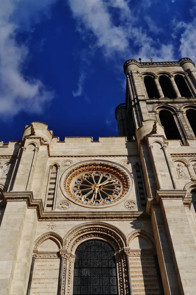 The Gothic choir and ambulatory of the Basilica of Saint-Denis, ranks of white marble royal tombs and recumbent gisants beneath soaring pointed arches and jewelled stained glass. Saint-Denis, France.